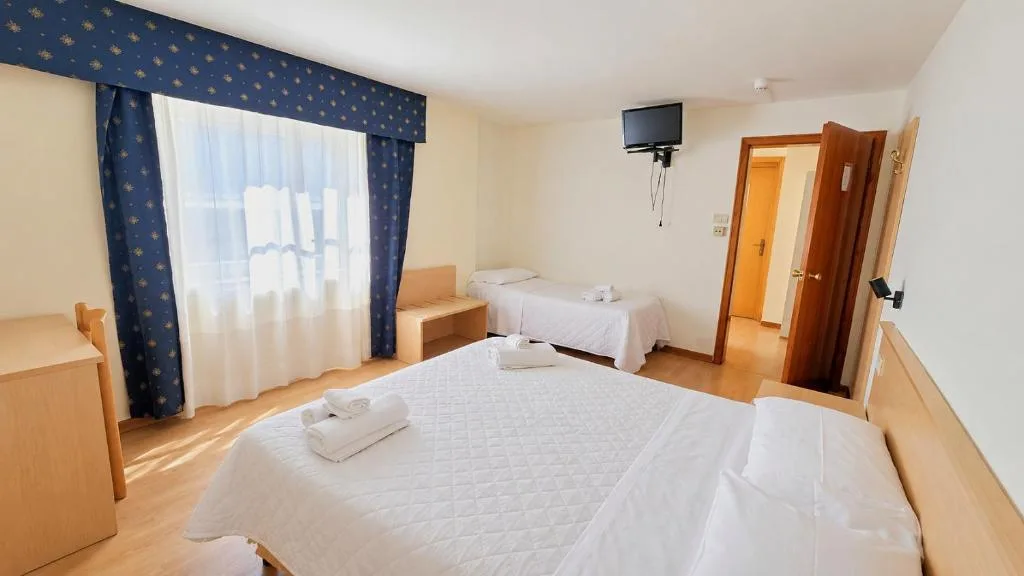 Camera tripla con letto matrimoniale, letto singolo, TV e tende blu