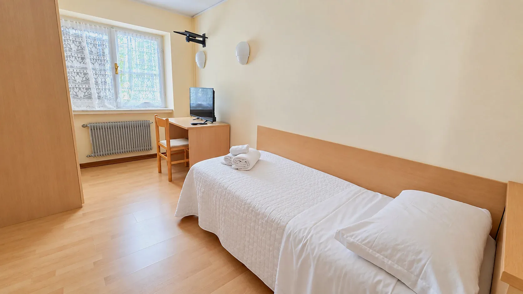 Camera singola con scrivania, TV, finestra e parquet