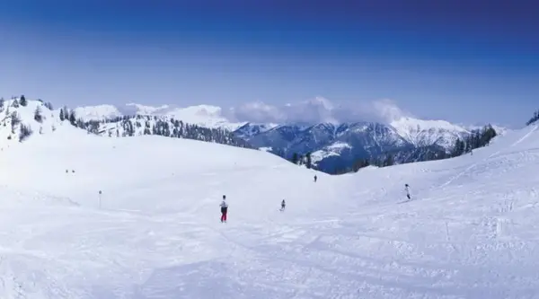 Pista da sci innevata con sciatori e panorama di montagne in lontananza