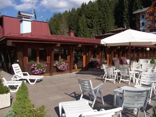Terrazza esterna con sedie bianche, ombrellone e fiori rosa davanti a edificio in legno