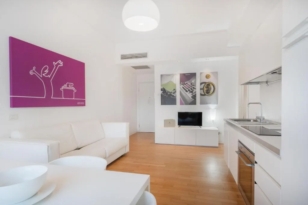 Soggiorno con divano bianco, angolo cottura, TV e quadri decorativi colorati