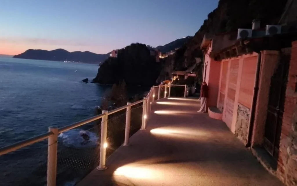 Passeggiata illuminata a picco sul mare al tramonto lungo la costa rocciosa