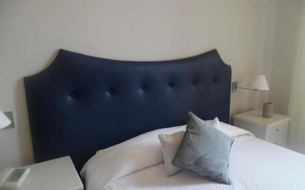 Dettaglio di letto con testiera imbottita blu, cuscini e comodino bianco con lampada