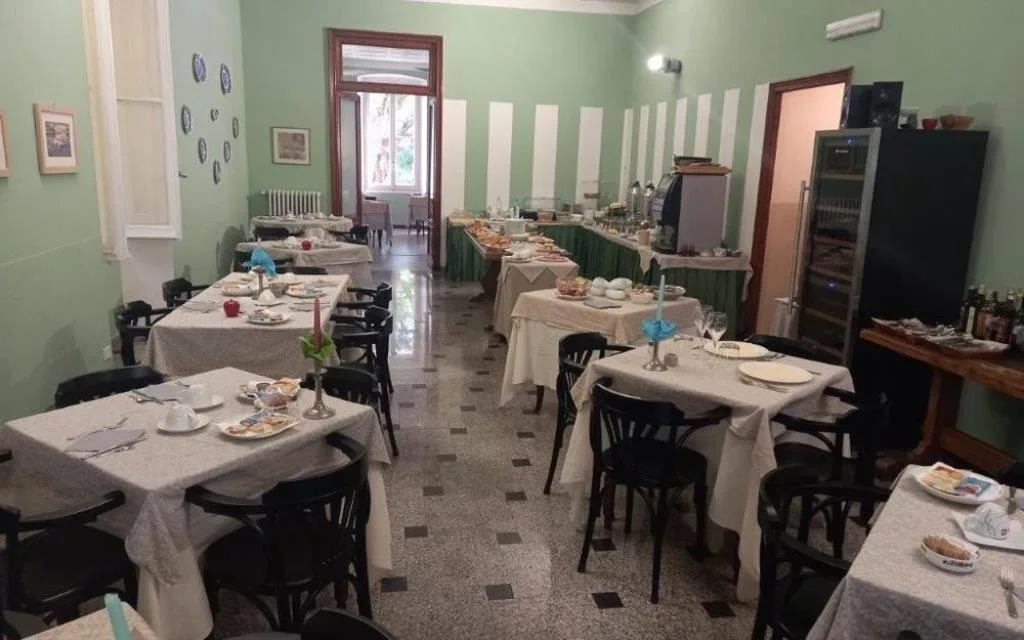 Sala colazione con pareti verdi, tavoli apparecchiati e buffet con prodotti