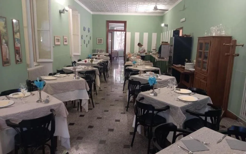 Sala ristorante con pareti verdi, tavoli apparecchiati e mobile in legno