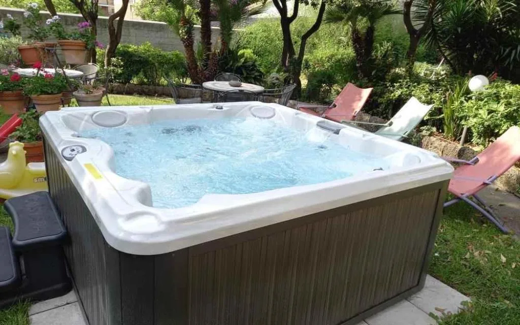 Vasca idromassaggio jacuzzi all'aperto nel giardino con sdraio e piante