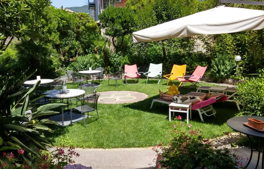 Giardino curato con prato verde, sdraie colorate, ombrellone e tavoli da esterno