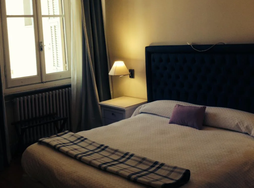 Camera con letto matrimoniale, testiera blu trapuntata, comodino e finestra con tende