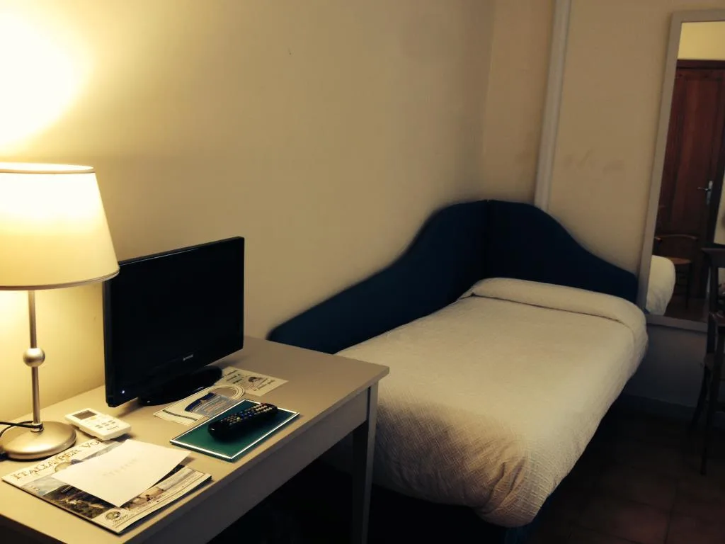 Camera singola con letto, scrivania bianca, TV e lampada accesa