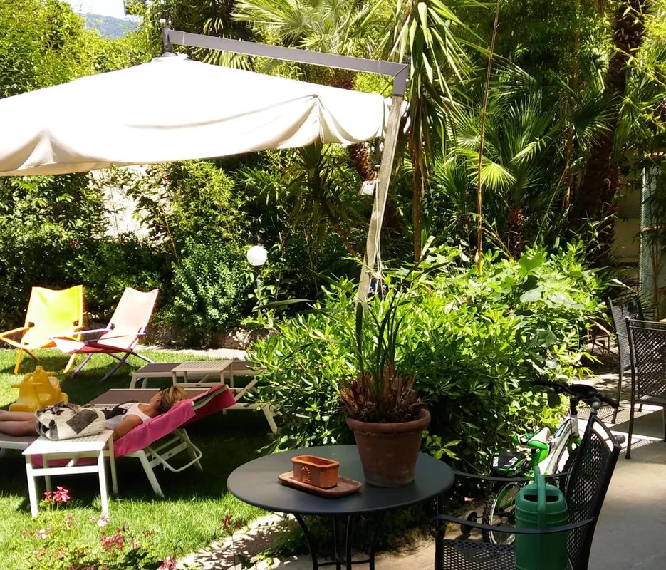 Giardino verde con sdraie colorate, ombrellone e vegetazione rigogliosa