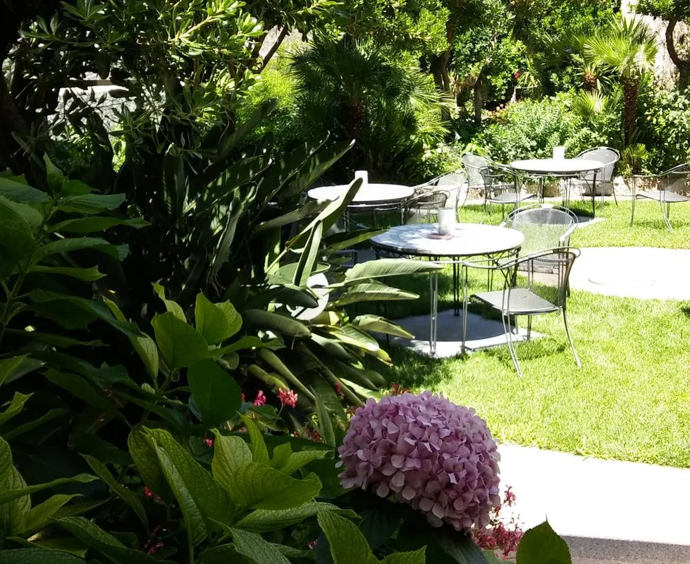 Giardino con tavoli, sedie in ferro e vegetazione fiorita con ortensia