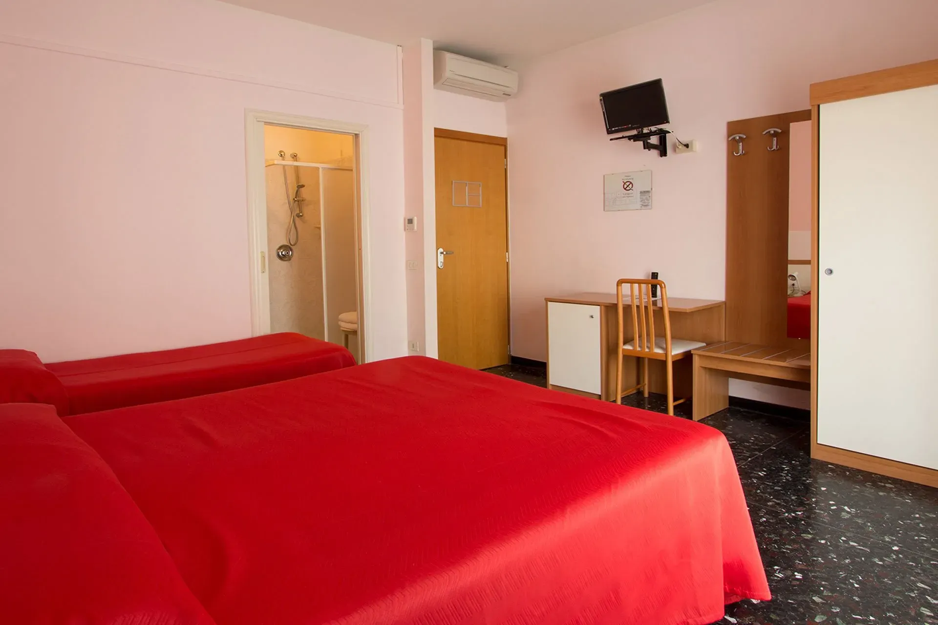 Camera con letto matrimoniale dalla coperta rossa, TV a parete e bagno con doccia