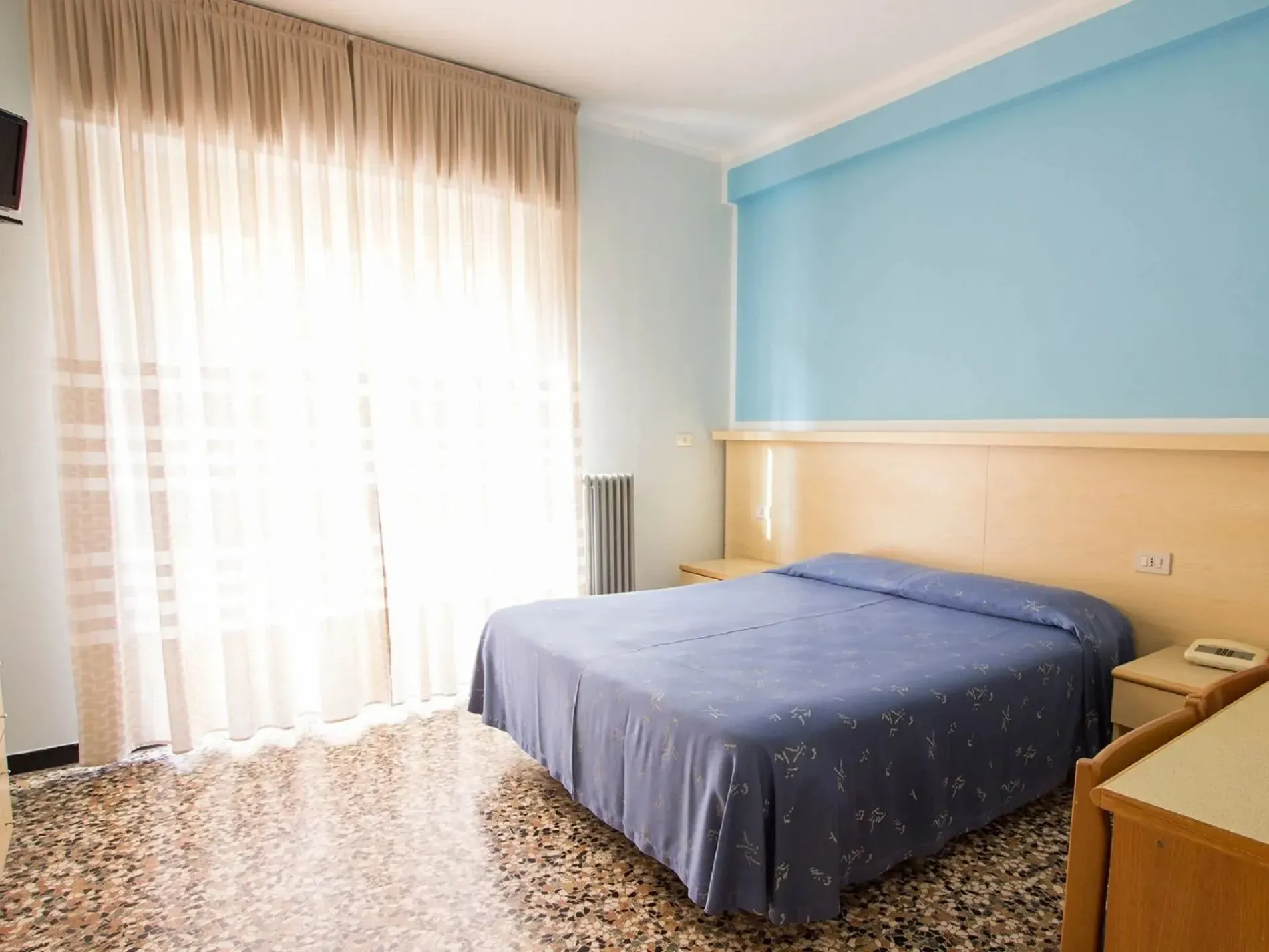 Camera matrimoniale con coperta azzurra, parete blu e ampia finestra con tende