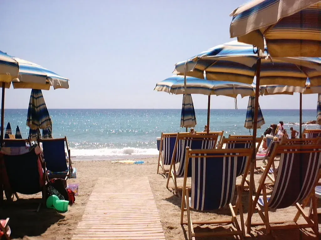 Spiaggia con ombrelloni a righe blu e gialle, sdraio e passerella verso il mare