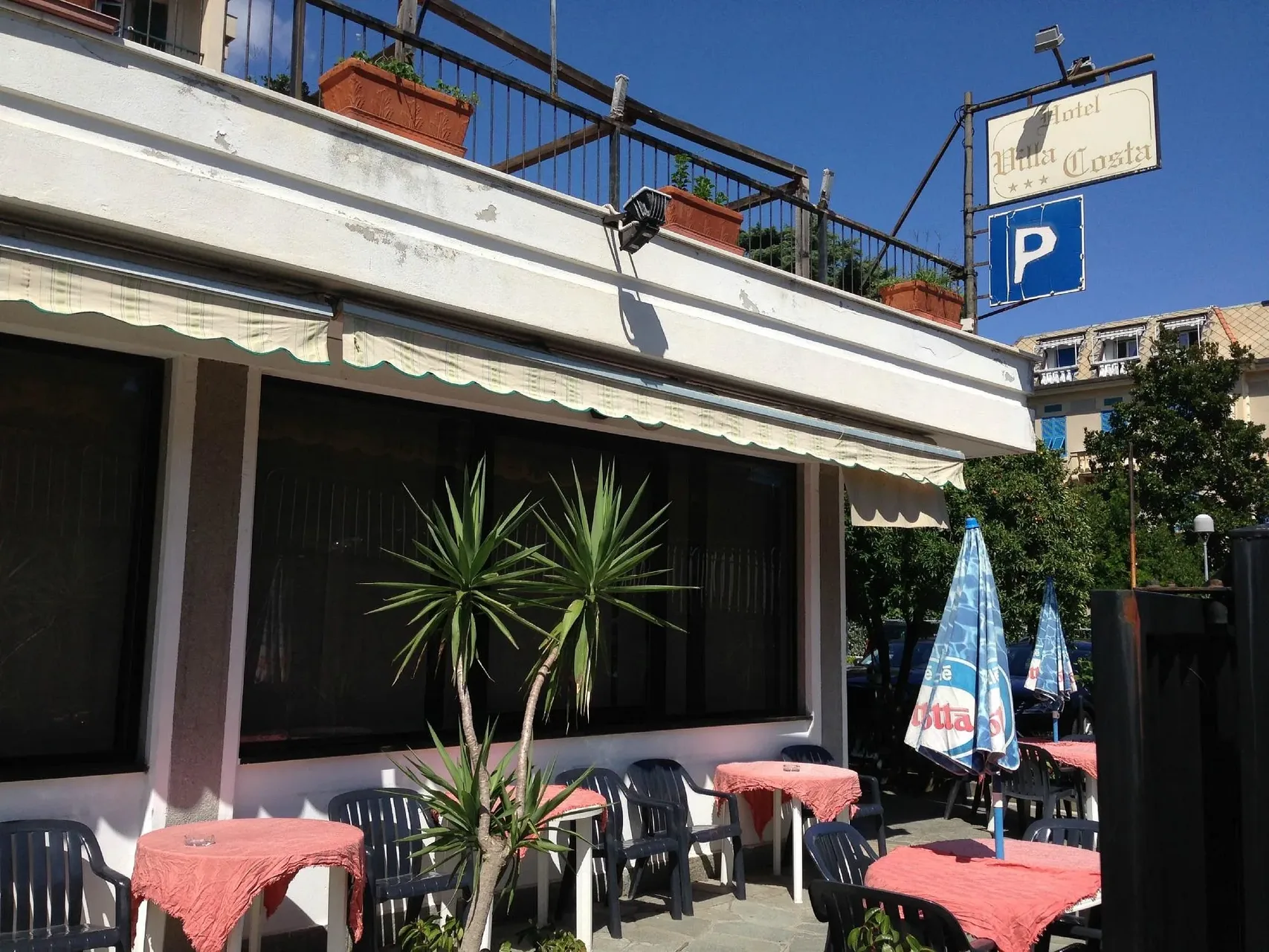 Terrazza esterna dell'hotel con tavolini, ombrelloni e insegna Villa Costa