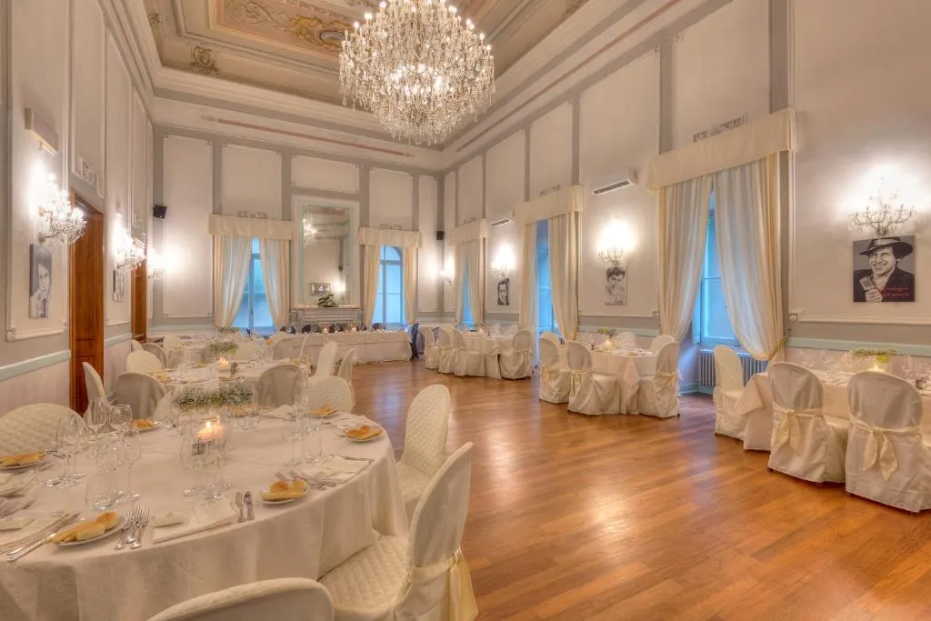 Elegante sala da ballo con lampadario di cristallo, tavoli allestiti e sedie con coprisedie bianchi