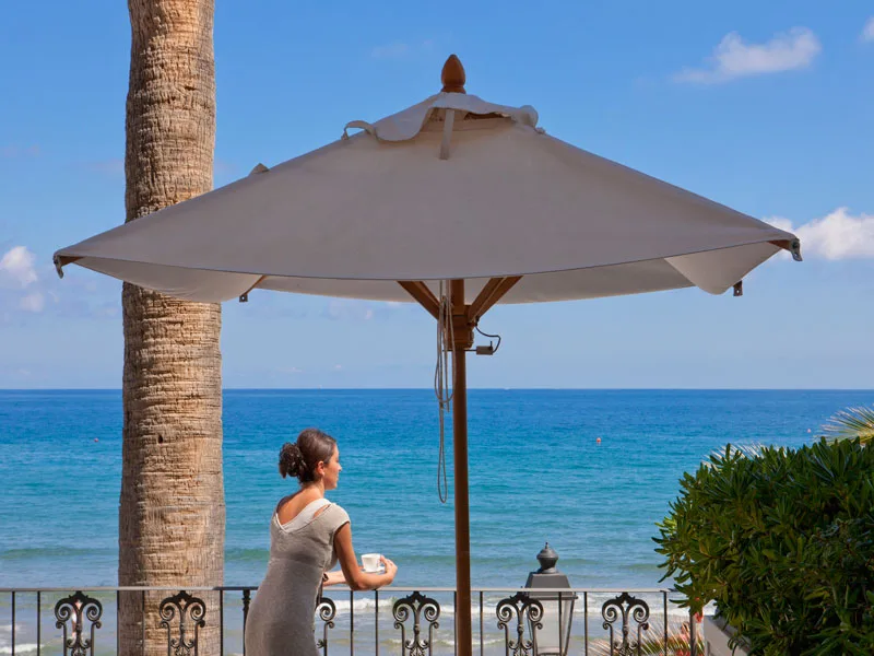 Donna sotto ombrellone su terrazza affacciata sul mare azzurro