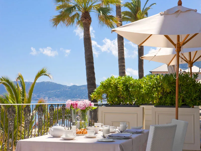 Terrazza con colazione, ombrellone e vista su palme e mare