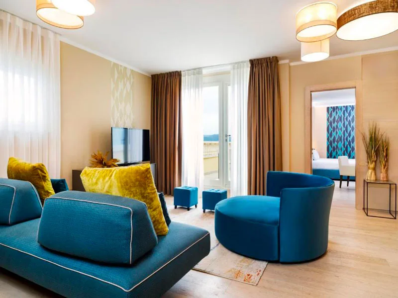 Soggiorno suite con divani blu, cuscini gialli e accesso al balcone