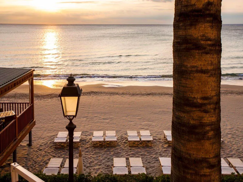 Tramonto sul mare con lampione, lettini sulla spiaggia e palma