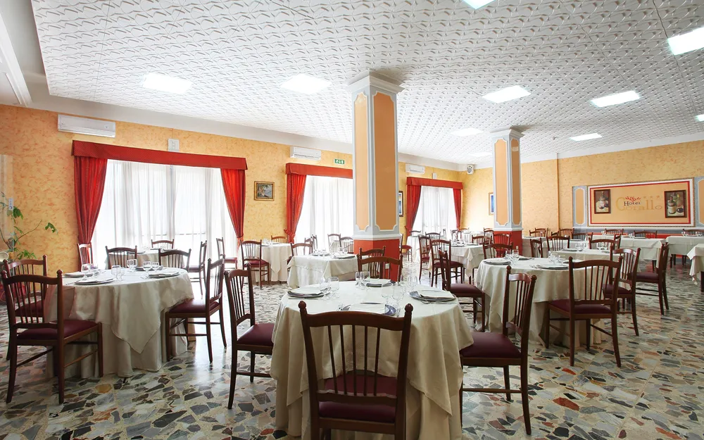 Sala da pranzo con tavoli apparecchiati, tende rosse e colonne decorate