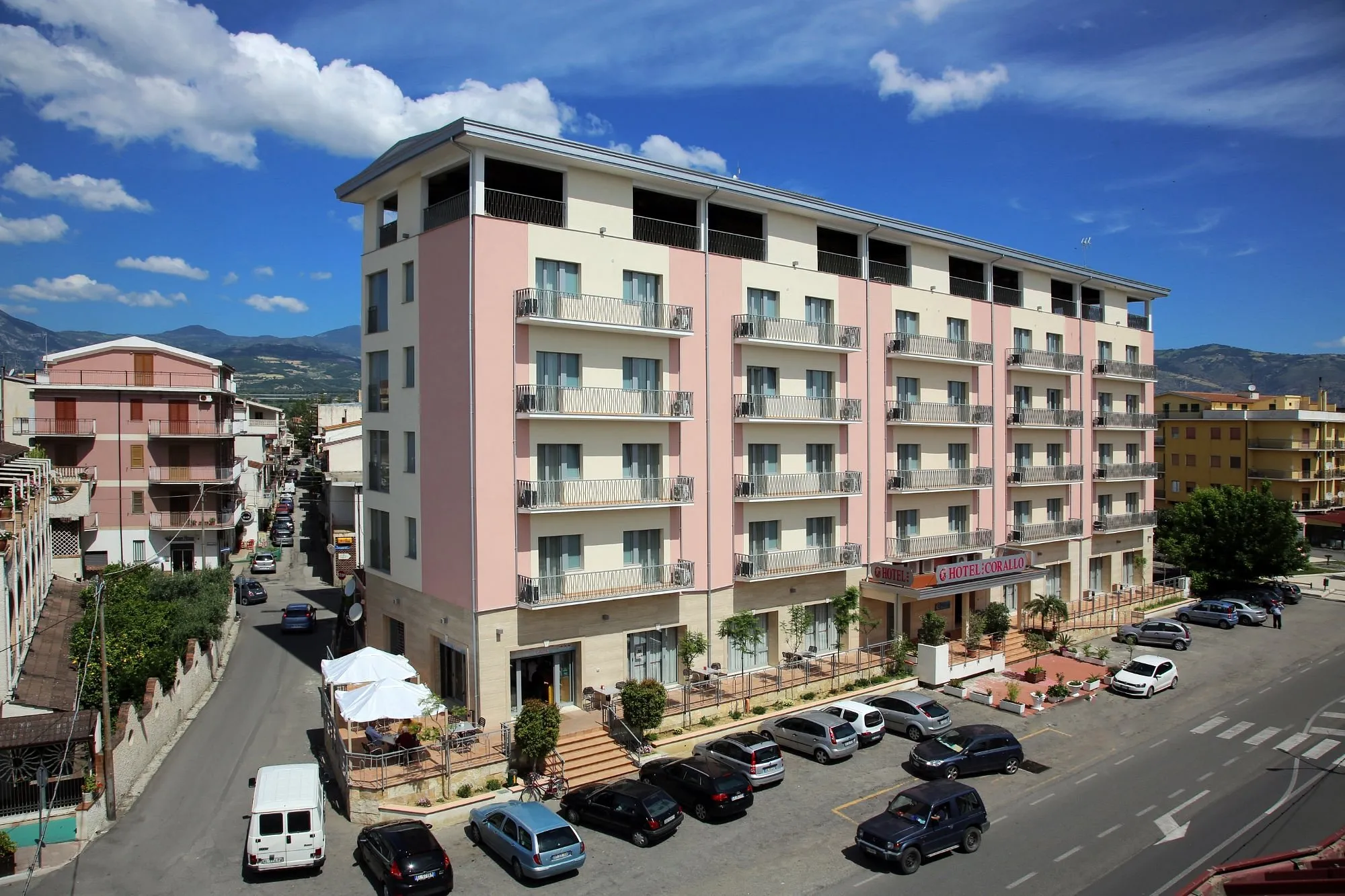 Vista panoramica dell'Hotel Corallo con parcheggio e montagne sullo sfondo