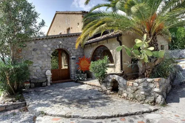 Ingresso in pietra di antico casale con arco, porta in legno e vegetazione mediterranea