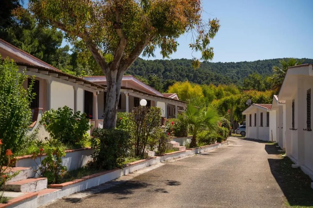 Viale interno del villaggio con bungalow bianchi, alberi e vegetazione con colline sullo sfondo