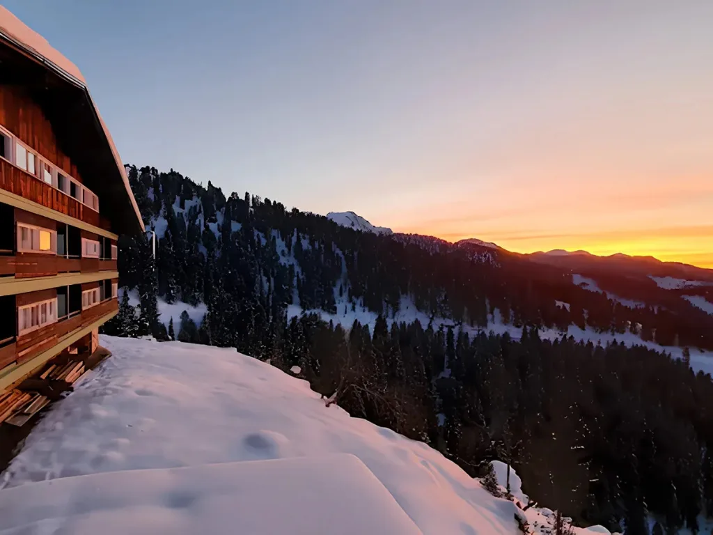 Facciata in legno dell'hotel con vista sulle montagne innevate al tramonto
