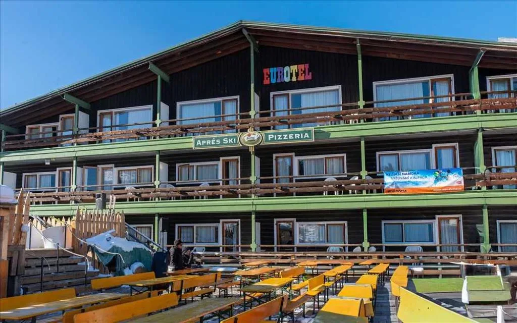 Facciata in legno dell'Eurotel con insegna Après Ski e Pizzeria e panche gialle