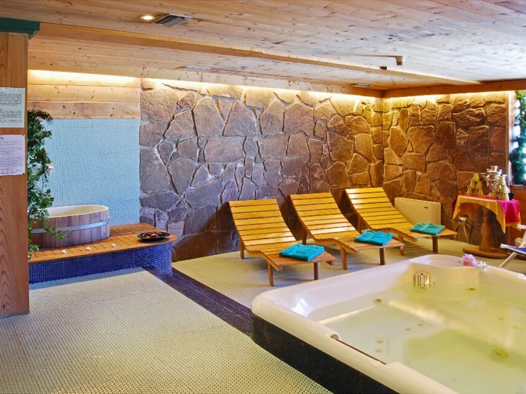 Area spa con vasca idromassaggio, lettini in legno e parete in pietra