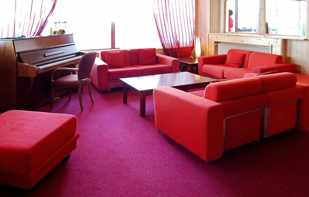 Salotto con divani rossi, pianoforte e moquette color magenta