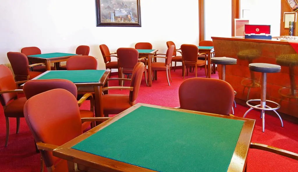 Sala giochi con tavoli da carte verdi e poltrone rosse