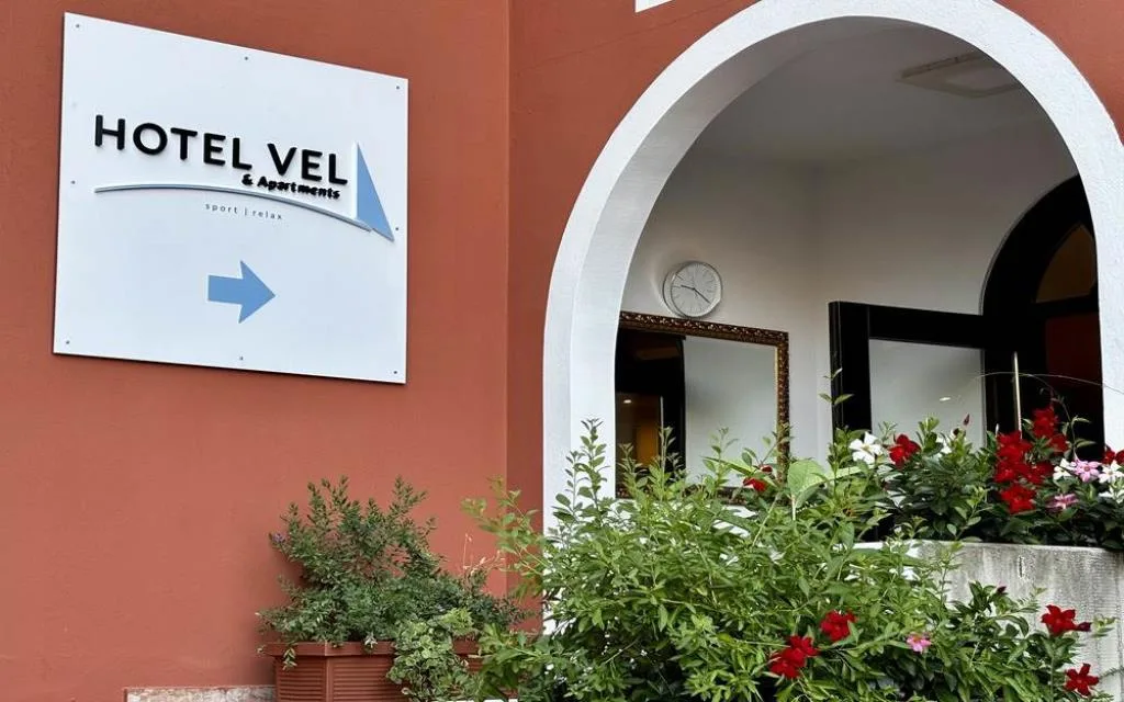 Insegna dell'Hotel Vel & Apartments con arco d'ingresso e piante fiorite
