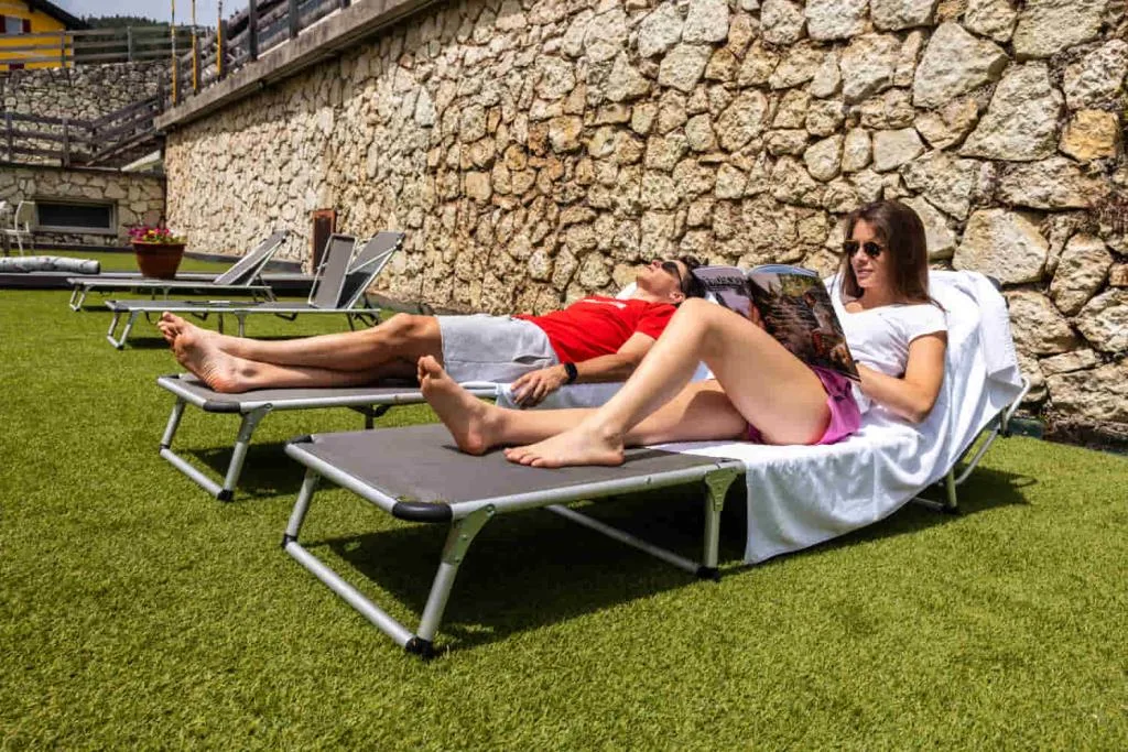 Coppia si rilassa sui lettini prendisole nel giardino con muro in pietra
