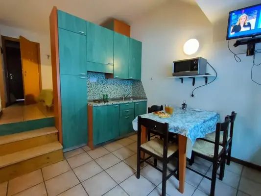 Cucina compatta verde con tavolo da pranzo, microonde e TV