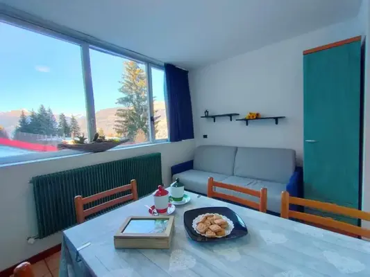 Soggiorno con tavolo da pranzo, divano grigio e ampia finestra con vista sulle montagne