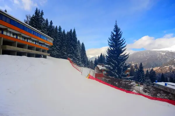 Esterno dell'hotel innevato con pista da sci e abeti sulle Alpi