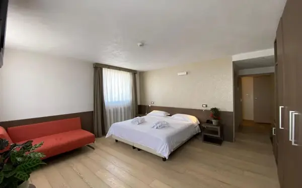 Ampia camera con letto matrimoniale, divano rosso e pavimento in parquet chiaro