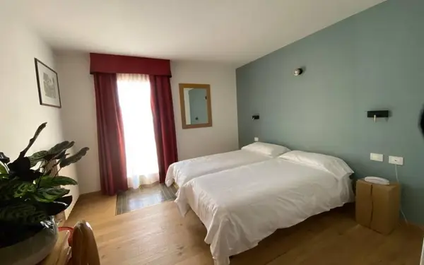 Camera doppia con parete verde acqua, letto bianco e tende rosse alla finestra