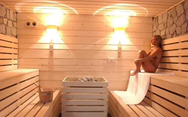 Interno della sauna in legno chiaro con illuminazione calda e persona seduta a rilassarsi