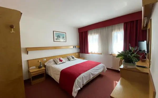 Camera matrimoniale con arredi in legno chiaro, copriletto rosso e tende rosse