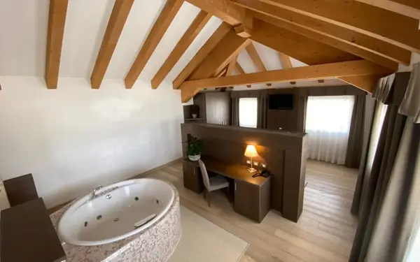 Camera mansardata con travi in legno a vista, vasca idromassaggio rotonda e scrivania