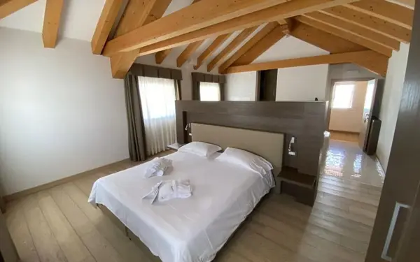 Camera con soffitto in travi di legno, letto matrimoniale con accappatoi e pavimento in parquet