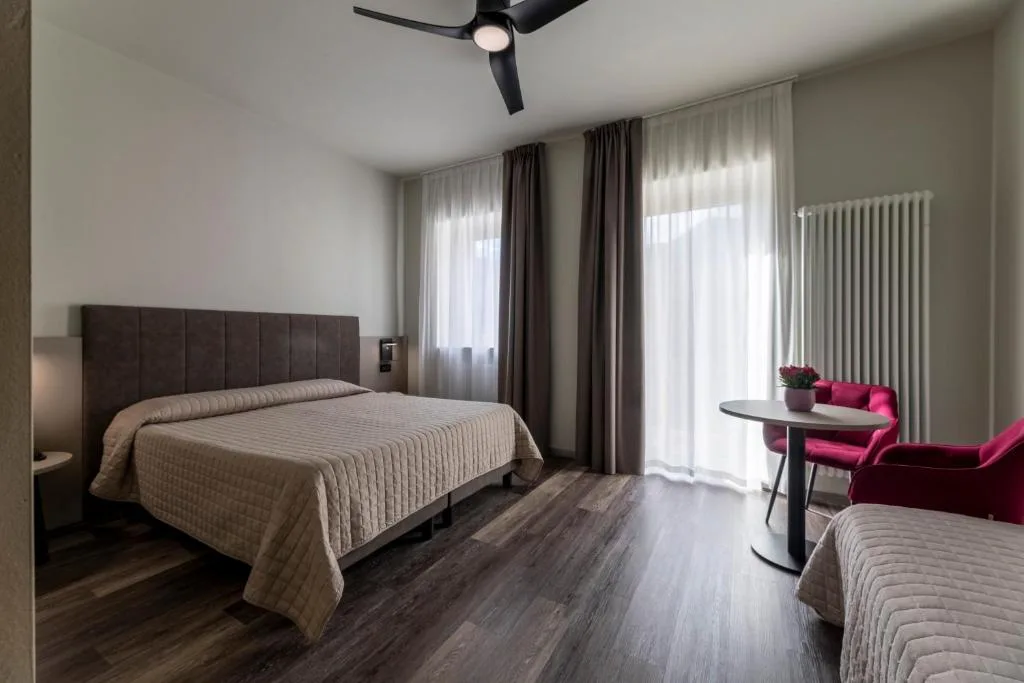 Camera moderna con letto, poltrone rosse, ventilatore a soffitto e tende