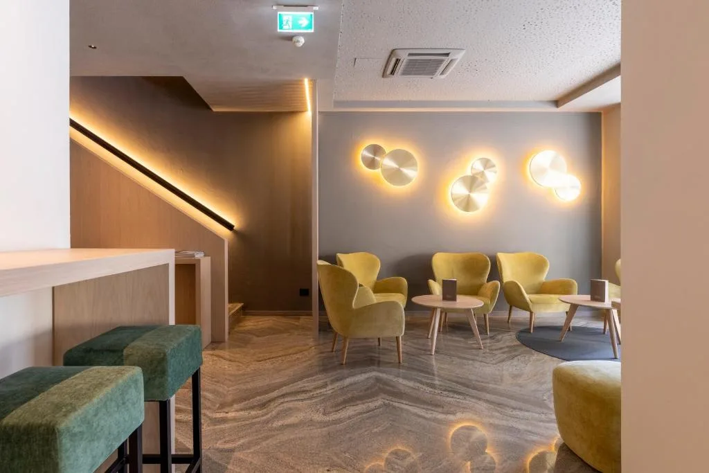 Area lounge con poltrone gialle, applique luminose e pavimento in marmo