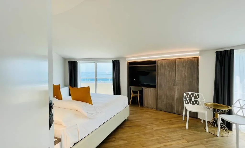 Camera luminosa con vista mare, letto e area soggiorno con sedie bianche