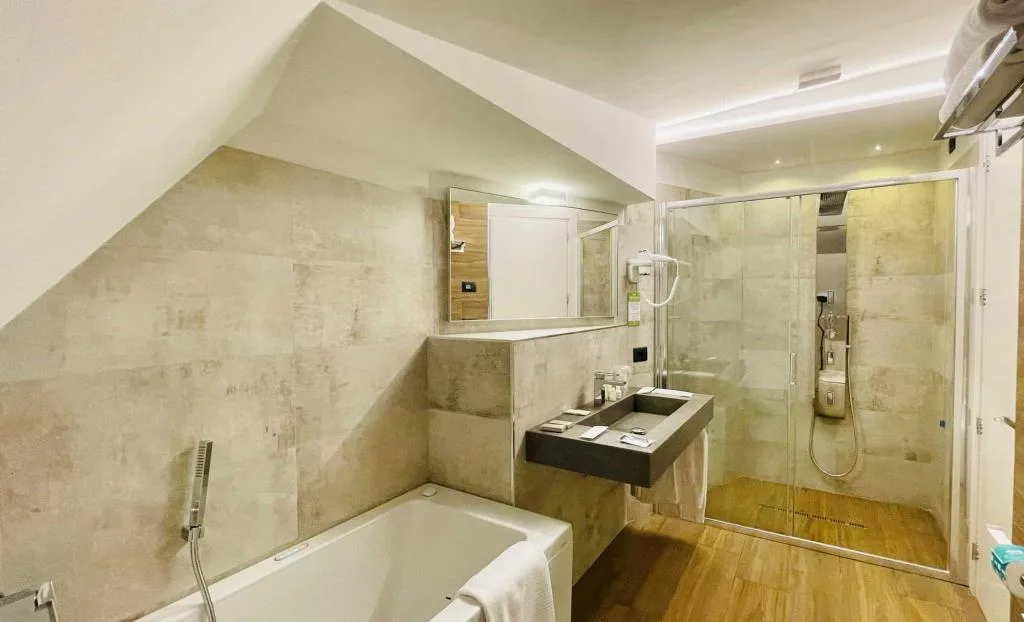 Bagno con vasca, doccia in vetro e lavabo su piastrelle beige