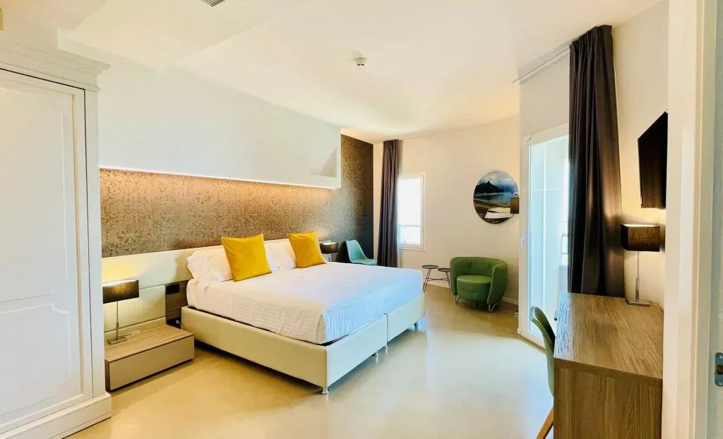 Suite ampia con letto, cuscini gialli, poltrona verde e balcone