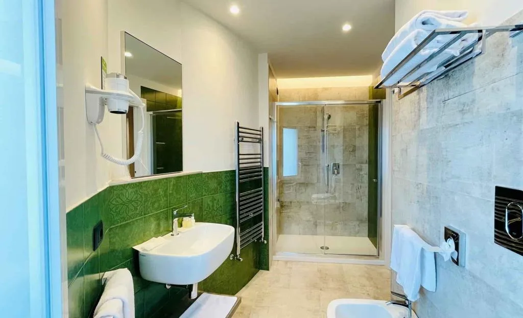 Bagno con doccia in vetro, lavabo e piastrelle verdi decorate